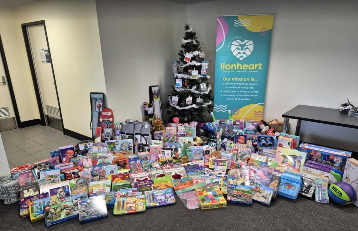 A large pile of wrapped Christmas donations in front of a decorated tree hung with tags, beside a Lionheart banner
