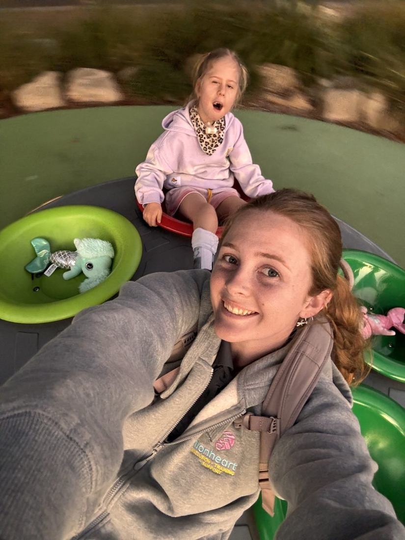 A Lionheart support worker on playground equipment with Florence, both laughing
