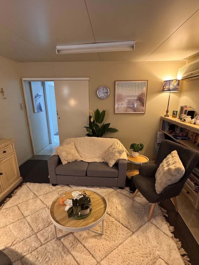 The doorway into the Brave Minds counselling room, with a two-seater couch, a clock, artwork and a pot plant