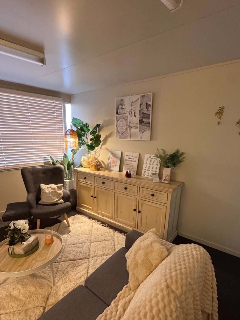 An armchair by the window beside a sideboard holding plants and a framed sign reading &lsquo;What you say in here stays in here&rsquo;