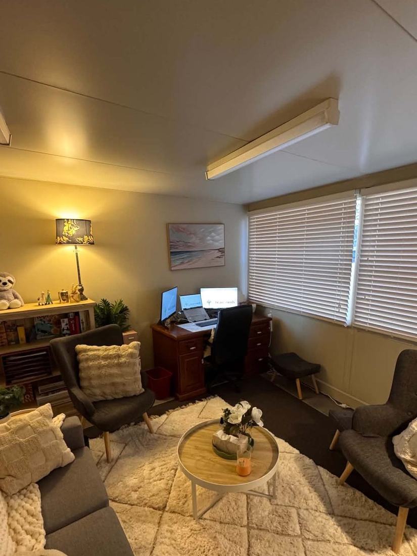 A wider view of the counselling room showing the couch, two armchairs, the rug and the desk in the corner