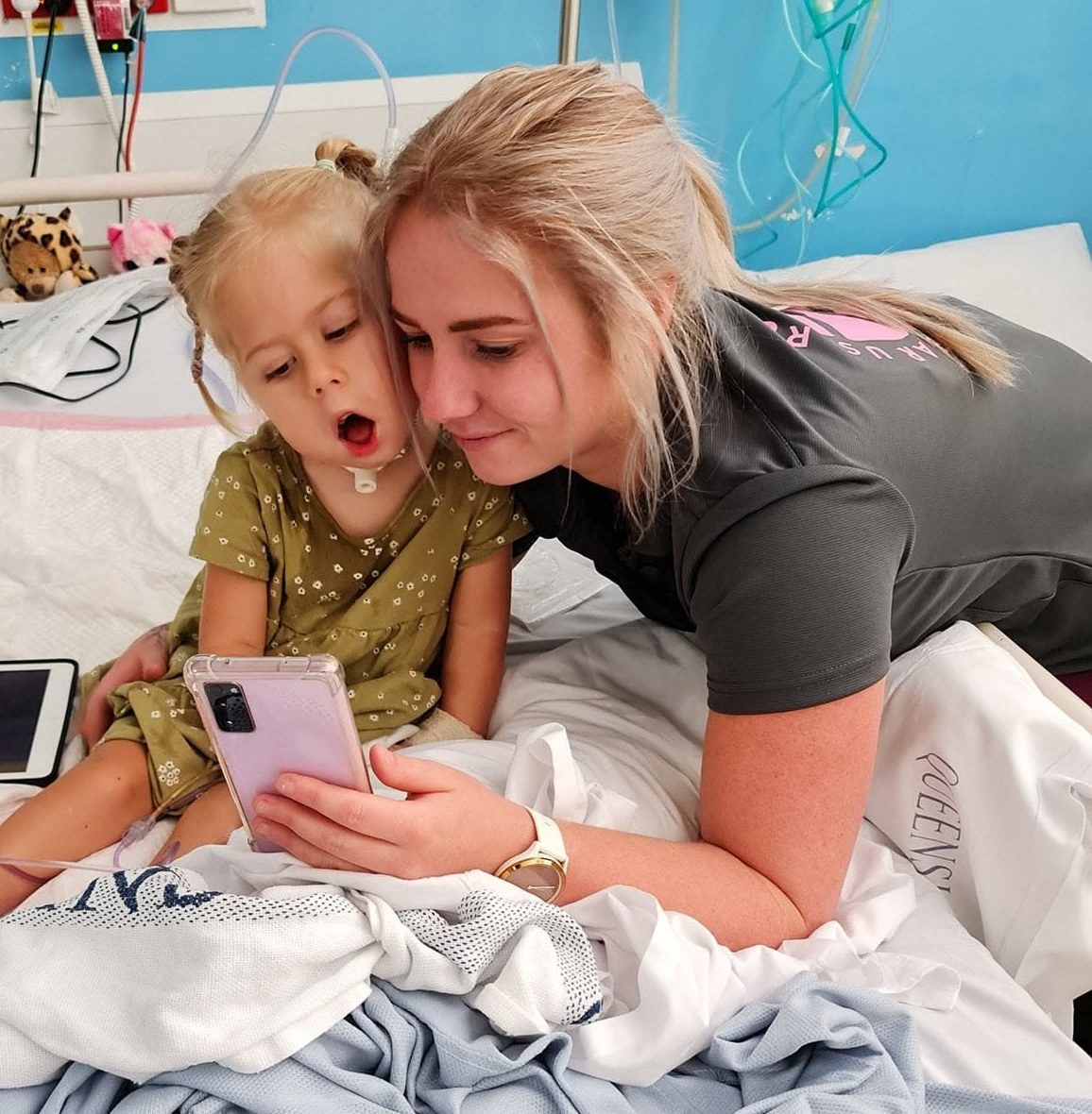 Kirstie, Lionheart's Operations Manager, lying on a hospital bed beside Florence, looking at a phone together